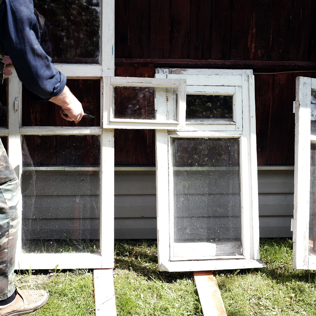 Person carrying TLC to old window frames leaning on the wooden wall of summer home